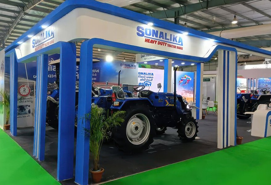 The stall as built on the show floor, a blue tractor under the canopy between branded pillars
